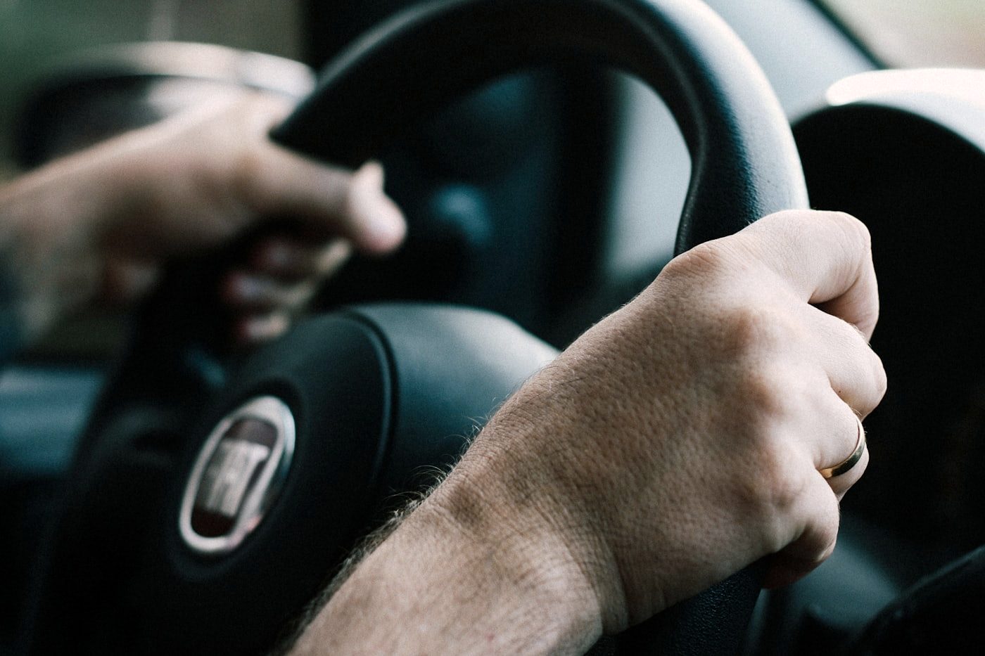 Two hands holding a steering wheel at the ten and two position.